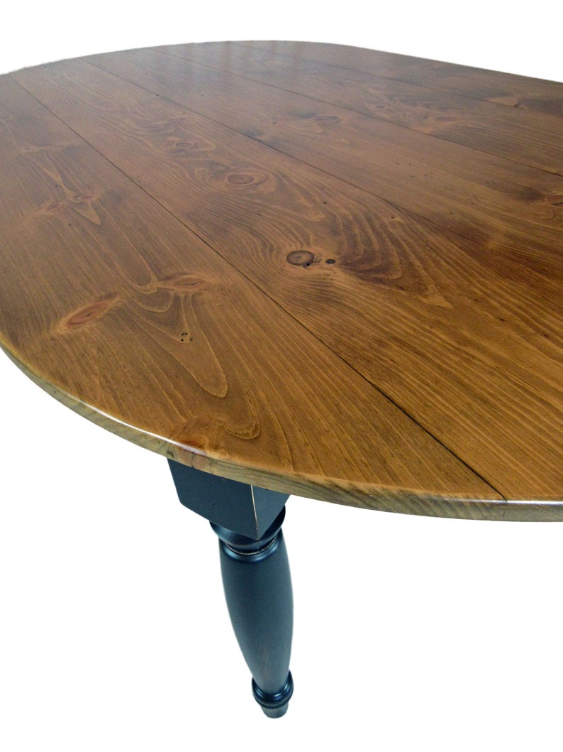 May include: A round dining table featuring a natural brown wood grain tabletop with visible knots and a smooth finish. The table is supported by a single, solid black turned leg that tapers toward the bottom, providing a stable base for the surface.