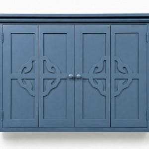May include: A blue cabinet with four doors and decorative cut-out designs. The cabinet has a rectangular shape with a crown molding top and two small round knobs for opening the doors. The cabinet is painted in a solid blue color.