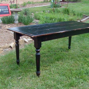 May include: Black farmhouse table with a distressed finish and turned legs. The table is made of wood and has a rectangular top. The table is sitting on a grassy lawn.
