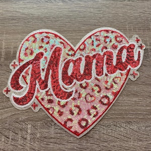 May include: A heart-shaped sequin patch with the word "Mama" in red script. The heart has a leopard print design in shades of red and pink, outlined with silver sequins. The patch is a decorative item.