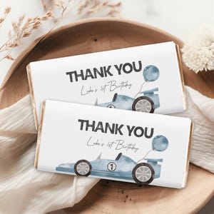 May include: Two white chocolate bar wrappers with blue race car designs and the text "Thank You Luke's 1st Birthday".