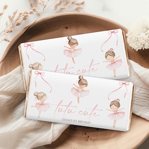 Puede incluir: Dos envoltorios blancos de barras de chocolate con temática de bailarina. Cada envoltorio presenta ilustraciones de bailarinas con tutús rosas, lazos rosas y el texto "tutu cute". También es visible el texto "Olivia's 1st Birthday".