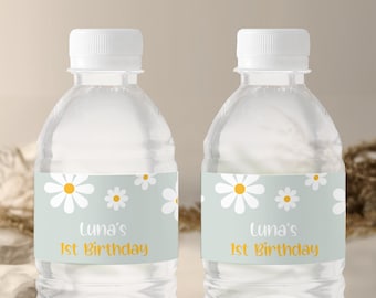 May include: Two clear plastic water bottles with white labels. The labels have a light blue background with white daisies and yellow centers. The text on the labels reads "Luna's 1st Birthday".