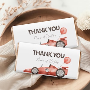 May include: Two white chocolate bar wrappers featuring a red racing car and a red balloon. The text on the wrappers reads "Thank You Noah's 1st Birthday".