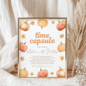 May include: A framed print with a gold border, featuring watercolor pumpkins and leaves. The text reads "time capsule" and "Autumn's 18th Birthday." The print is designed to be opened later, with space for messages.