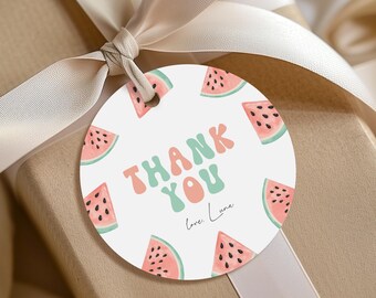 Peut inclure: Une étiquette cadeau ronde avec un motif de tranches de pastèque et les mots "THANK YOU" en rose et vert. L'étiquette est attachée à un cadeau emballé avec un ruban crème.