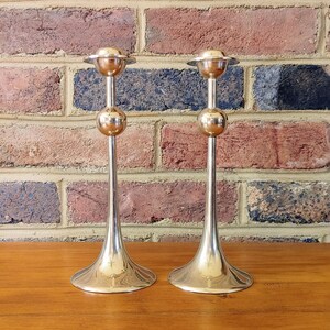 May include: Two silver candle holders with a round base and a round top. The candle holders are on a wooden surface.