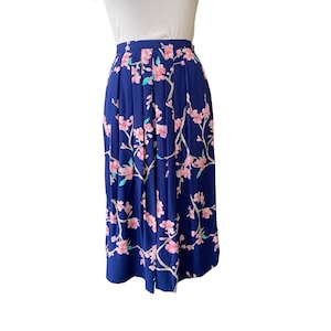 May include: A navy blue pleated skirt featuring a floral pattern of pink blossoms and white branches. The skirt has a high waist and falls to the mid-calf. The floral design is evenly distributed across the fabric, creating a visually appealing garment.