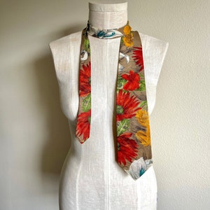 May include: A brown silk tie with a floral pattern featuring red, yellow, and green flowers. The tie is on a white mannequin.