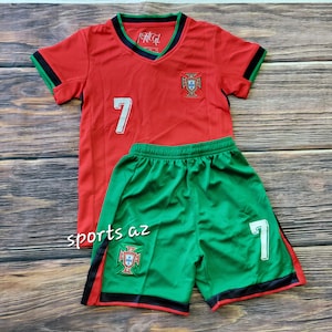 May include: Red and green soccer jersey and shorts set with the number 7 and the Portuguese national team crest. The jersey has black trim on the sleeves and collar. The shorts have black trim on the waistband and legs.