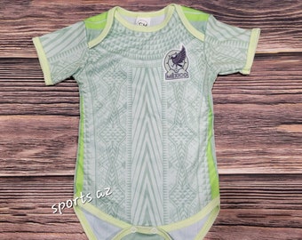 May include: A light green baby onesie with a geometric pattern and a green and black patch that says "Mexico" with a bird design.