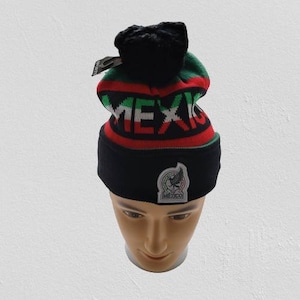 May include: Black knit beanie with a pom pom on top. The beanie has a red, white, and green stripe pattern with the word "MEXICO" in white letters. A small white patch with a black eagle and the word "MEXICO" is on the front.