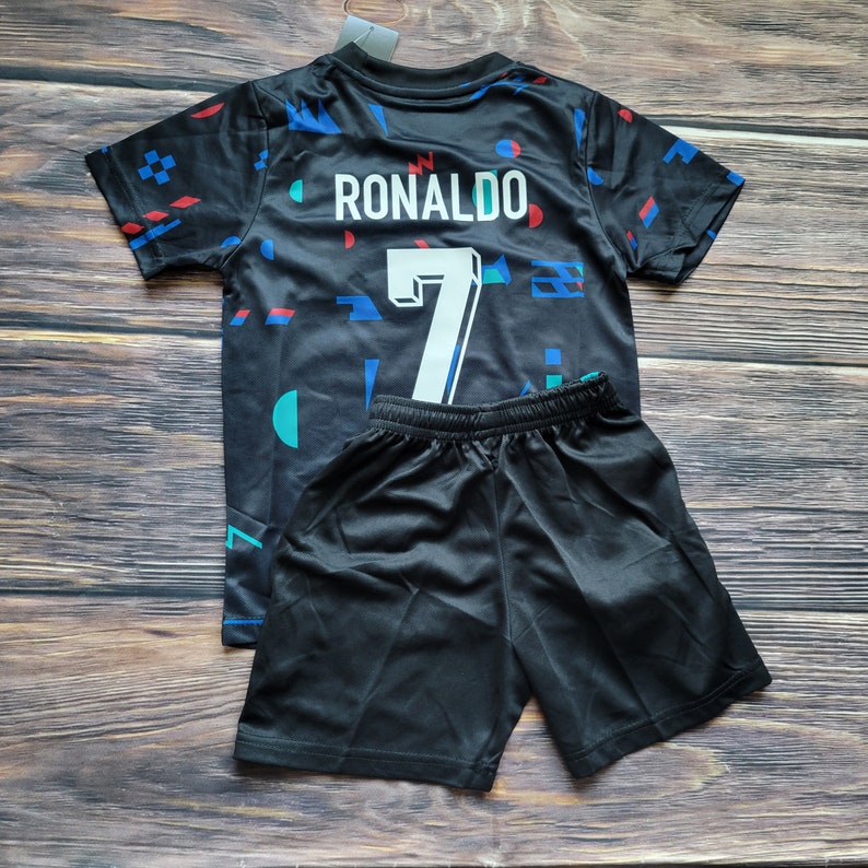 May include: Black soccer jersey with a geometric pattern and the name "RONALDO" and the number "7" on the back. The jersey is paired with black shorts.