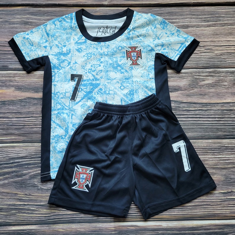 May include: A blue and white soccer jersey with the number 7 and the Portuguese crest. The jersey is paired with black soccer shorts with the number 7 and the Portuguese crest.
