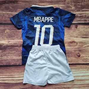 May include: A blue and black patterned soccer jersey with the name MBAPPE and the number 10 printed in white on the back, paired with plain white athletic shorts. The jersey features short sleeves and a dark blue collar with white trim.