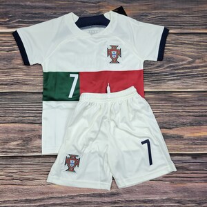 May include: White soccer jersey and shorts set with the Portuguese national team crest and the number 7. The jersey has a green and red stripe across the chest.