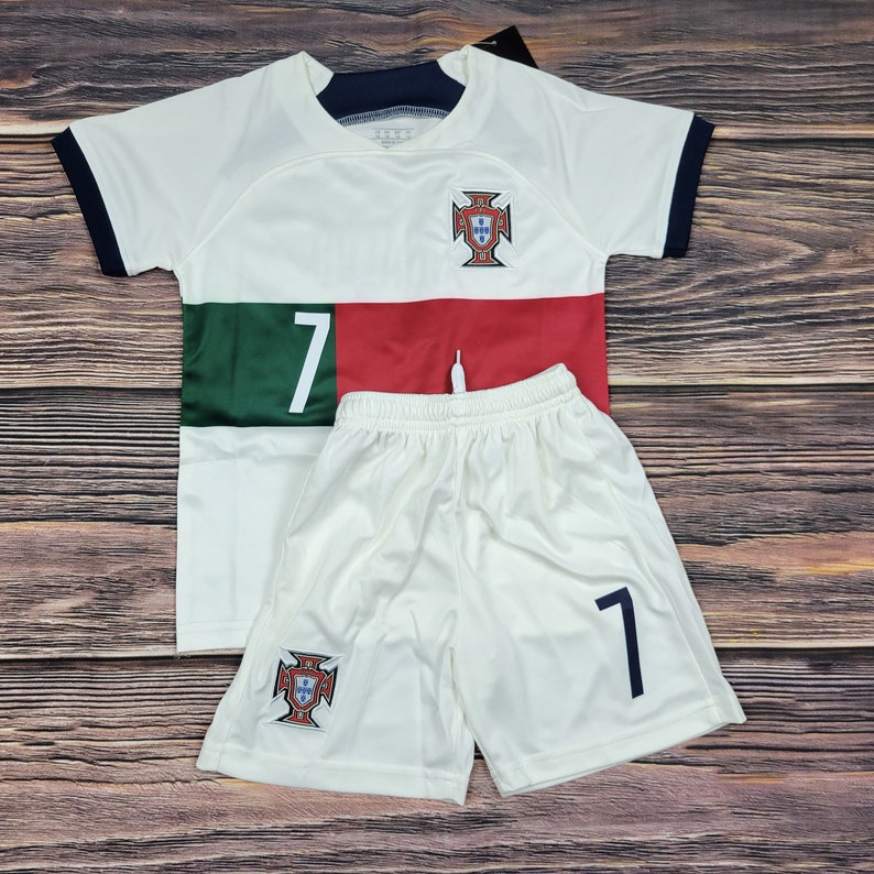 May include: White soccer jersey and shorts set with the Portuguese national team crest and the number 7. The jersey has a green and red stripe across the chest.