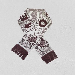 May include: White and brown knitted scarf with a brown eagle and the word "MEXICO" on each end. The scarf has a white background with a brown pattern.