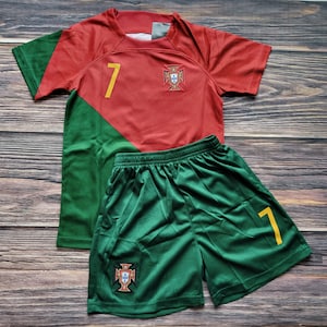 May include: A red and green soccer jersey with the number 7 and the Portuguese crest. The jersey is paired with green soccer shorts with the number 7 and the Portuguese crest.