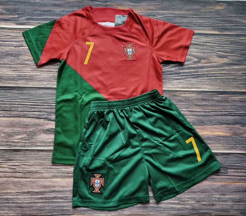 May include: A red and green soccer jersey with the number 7 and the Portuguese crest. The jersey is paired with green soccer shorts with the number 7 and the Portuguese crest.
