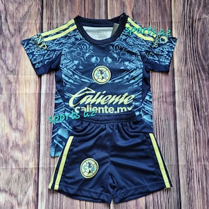 May include: A navy blue soccer uniform set featuring a jersey and shorts. The jersey has yellow accents and the word "Caliente" printed on the front. The shorts have yellow stripes and a team logo.