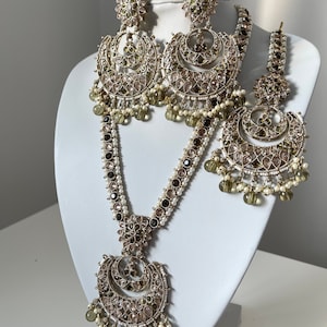 May include: A gold necklace and earrings set with a crescent moon design. The jewelry is adorned with clear and green stones, and white pearls.