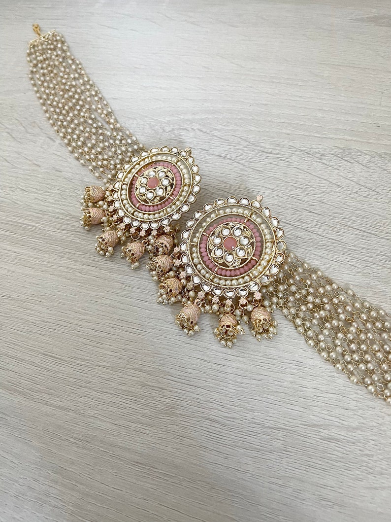 May include: A pair of large, round, gold earrings with pink and white stones and pearl accents. The earrings have a dangling design with multiple layers of pearls.
