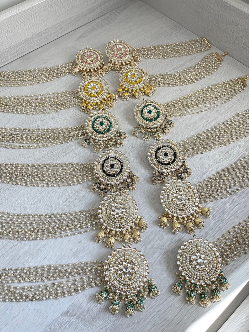 May include: A set of eight pairs of gold-tone earrings with pearl and gemstone accents. The earrings feature a round design with a central gemstone surrounded by smaller pearls and gemstones. The earrings are arranged in rows, with each row featuring a different color gemstone: pink, yellow, green, black, and white.