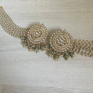 May include: A pair of large, round, gold earrings with white pearls and green accents. The earrings have a delicate, intricate design and are perfect for a special occasion.