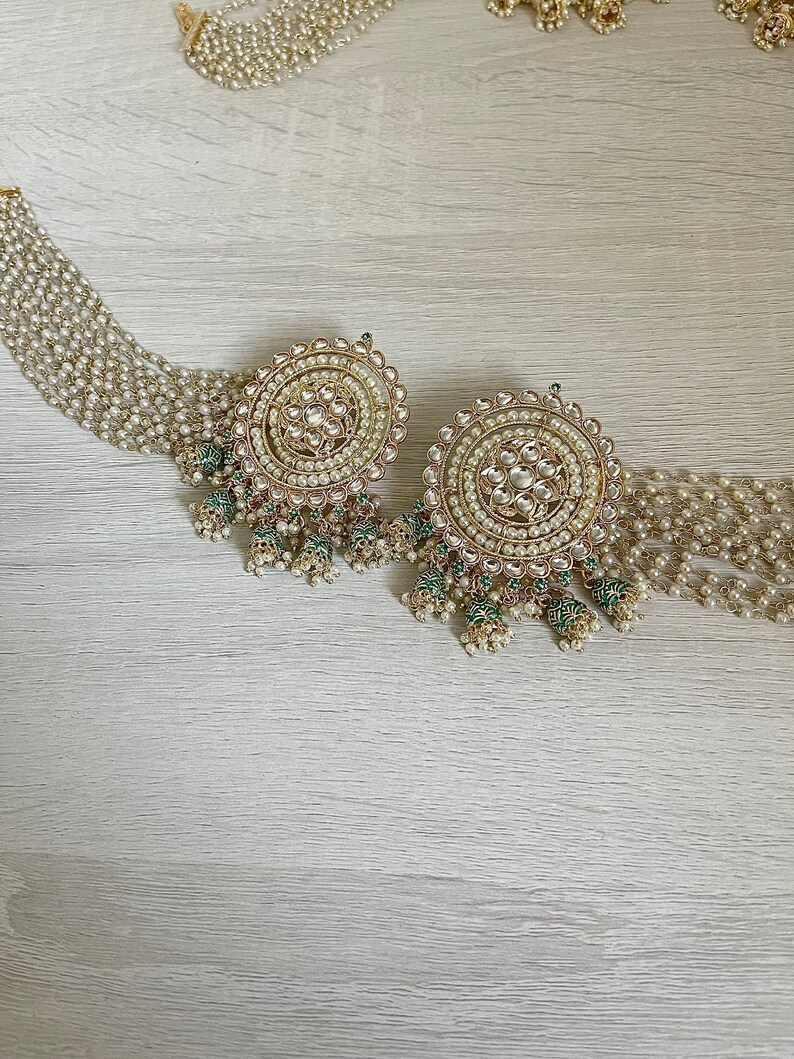 May include: A pair of large, round, gold earrings with white pearls and green accents. The earrings have a delicate, intricate design and are perfect for a special occasion.
