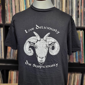 May include: Black t-shirt with a white graphic of a ram's head with the text "Live Deliciously Die Suspiciously" printed on the front.