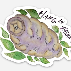 May include: A watercolor illustration of a tardigrade, also known as a water bear, surrounded by green leaves. The tardigrade is purple and brown with a white eye. The text "HANG IN THERE" is written in purple above the tardigrade.