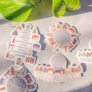 Op de afbeelding: Vijf kleurrijke stickers met een wereldbol met verschillende gebouwen eromheen. De stickers hebben de tekst "WORLD TRAVELER" en lijst landen op zoals Mexico, Noorwegen, China, Duitsland, Itali&euml;, de Verenigde Staten, Japan, Marokko, Frankrijk, het Verenigd Koninkrijk en Canada.
