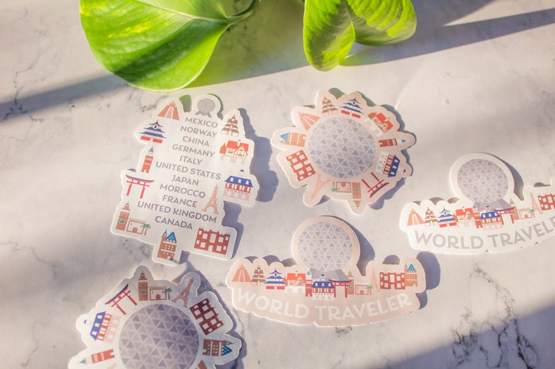 Op de afbeelding: Vijf kleurrijke stickers met een wereldbol met verschillende gebouwen eromheen. De stickers hebben de tekst "WORLD TRAVELER" en lijst landen op zoals Mexico, Noorwegen, China, Duitsland, Itali&euml;, de Verenigde Staten, Japan, Marokko, Frankrijk, het Verenigd Koninkrijk en Canada.
