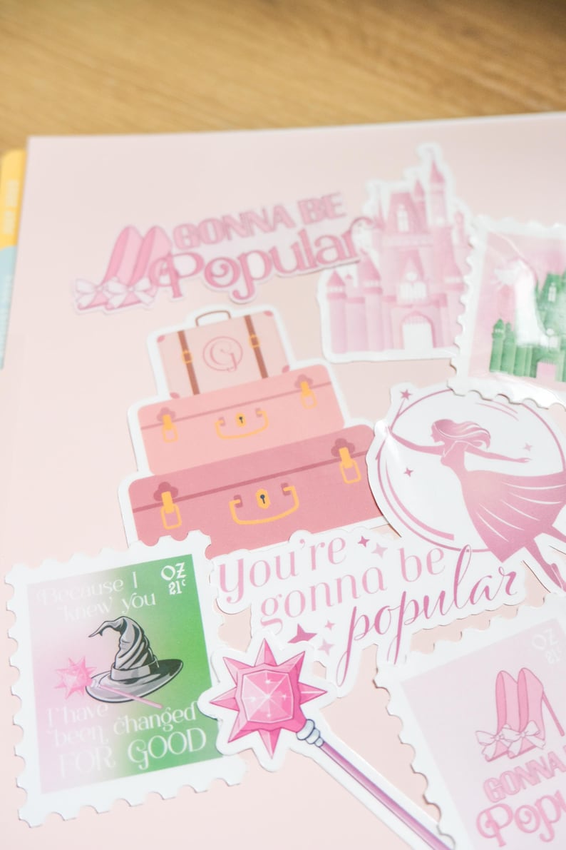 Op de afbeelding: Roze stickers met de tekst "Gonna Be Popular" en andere zinnen. De stickers tonen afbeeldingen van koffers, een kasteel, een heksenhoed, een toverstaf en een silhouet van een vrouw. Op een roze achtergrond.