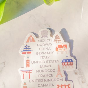 Op de afbeelding: Een witte sticker met kleurrijke illustraties van bezienswaardigheden uit verschillende landen over de hele wereld. De sticker bevat de tekst "Mexico, Noorwegen, China, Duitsland, Itali&euml;, Verenigde Staten, Japan, Marokko, Frankrijk, Verenigd Koninkrijk, Canada".