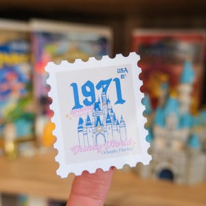 Pode incluir: Um selo postal branco com uma ilustra&ccedil;&atilde;o azul de um castelo e o texto "1971" e "Disney World Orlando, Florida". O selo tamb&eacute;m tem o texto "USA 21&cent;".