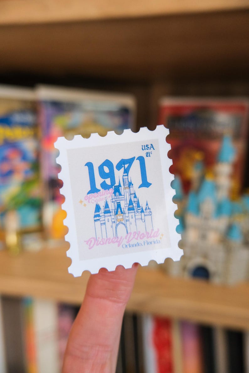 Pode incluir: Um selo postal branco com uma ilustra&ccedil;&atilde;o azul de um castelo e o texto "1971" e "Disney World Orlando, Florida". O selo tamb&eacute;m tem o texto "USA 21&cent;".