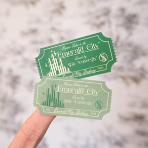 Op de afbeelding: Twee groene en lichtgroene "Express Ticket to the Emerald City" tickets. De tickets zijn rechthoekig met afgeronde hoeken en bevatten de tekst "Issued by: Shiz University" en "Emerald City Railway".