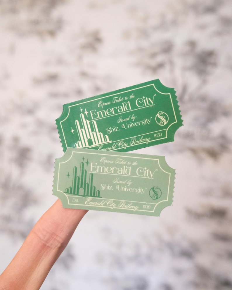 Op de afbeelding: Twee groene en lichtgroene "Express Ticket to the Emerald City" tickets. De tickets zijn rechthoekig met afgeronde hoeken en bevatten de tekst "Issued by: Shiz University" en "Emerald City Railway".