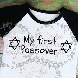 May include: White and black long-sleeved shirt with a black Star of David and the text "My first Passover" on the front.