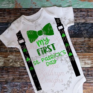 May include: White baby onesie with black suspenders and a green bow tie. The onesie has the text "My First St. Patrick's Day" printed on it.