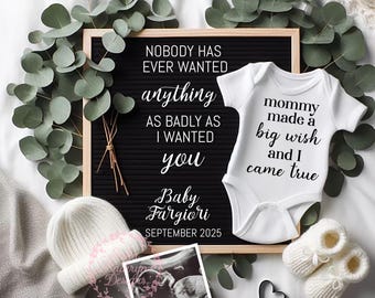 May include: A white onesie with the text "mommy made a big wish and I came true" on it. A black letter board with the text "NOBODY HAS EVER WANTED anything AS BADLY AS I WANTED you Baby Fargiori SEPTEMBER 2025". A white knitted hat, a pair of white booties, a black heart, and a sonogram image are also in the image.