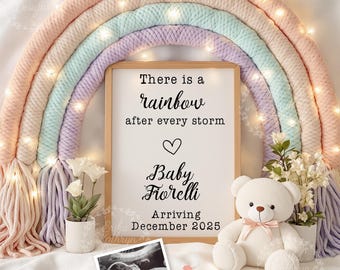 Può includere: Un cartello bianco con testo nero che recita "There is a rainbow after every storm" con un simbolo di cuore. Sotto il testo c'è "Baby Fiorelli" e "Arriving December 2025". Un orsacchiotto bianco con un fiocco rosa è seduto davanti al cartello. Un arcobaleno fatto di corda color pastello con luci bianche è sullo sfondo.
