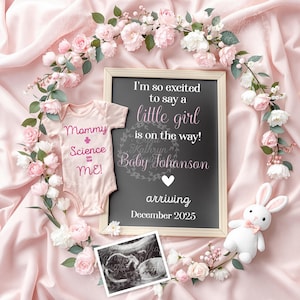 May include: A pink and white floral arrangement surrounds a chalkboard sign announcing the arrival of a baby girl in December 2025. The sign reads "I'm so excited to say a little girl is on the way! Baby Johanson arriving December 2025". A pink onesie with the text "Mommy + Science ME!" is also included in the image.