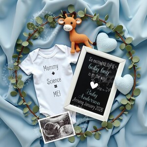May include: A white onesie with the text "Mommy + Science = ME!"  A framed chalkboard sign with the text "So excited to say a baby boy is on the way! Baby Anderson Arriving January 2026". A blue blanket with a stuffed giraffe toy and a blue heart.