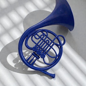 May include: A vibrant blue French horn, a brass instrument, is displayed against a light background. The horn's coiled tubing and bell are clearly visible, casting a shadow. The instrument's design is detailed, showcasing its curves and valves.