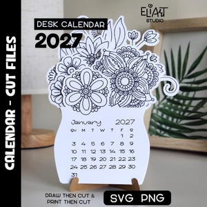 May include: A white paper desk calendar for 2027 featuring a black and white floral illustration at the top. The calendar displays the month of January 2027 with dates arranged in a grid. It is supported by a small brown wooden stand base.