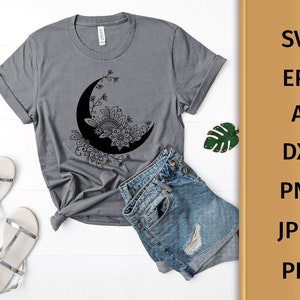 May include: A gray t-shirt with a black and white floral design of a crescent moon. The design is intricate and detailed, with a floral pattern surrounding the moon.