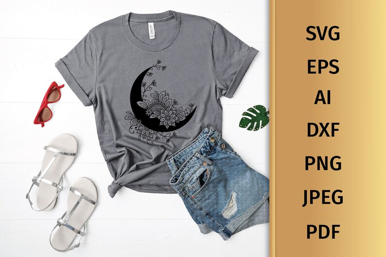 May include: A gray t-shirt with a black and white floral design of a crescent moon. The design is intricate and detailed, with a floral pattern surrounding the moon.